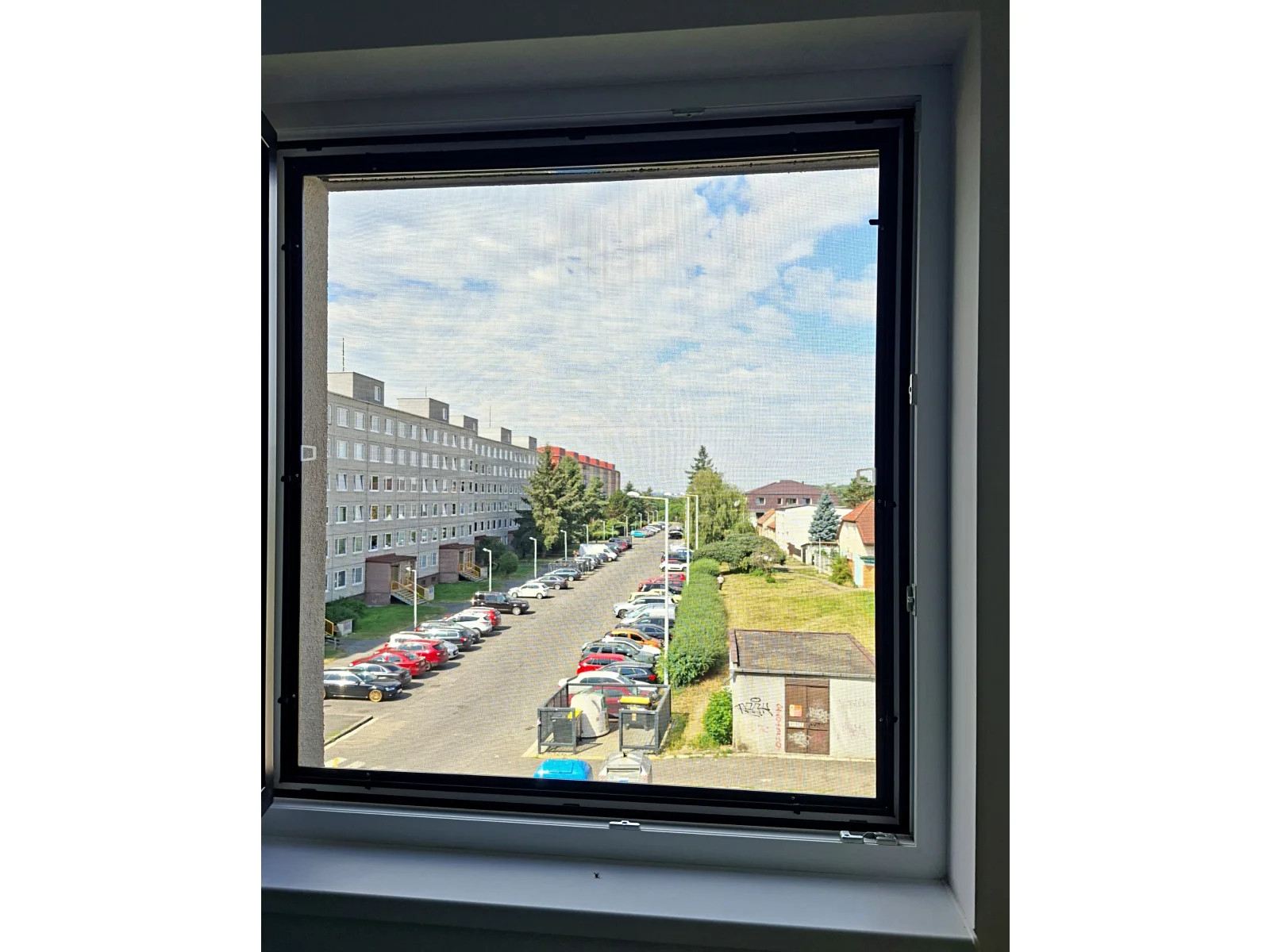 Pohled přes černou síťovinu pevné sítě v otevřeném okně v Libuši